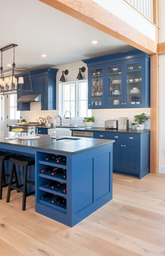 Mid-sized cottage single-wall light wood floor eat-in kitchen photo in Boston with a farmhouse sink, shaker cabinets, blue cabinets, soapstone countertops, white backsplash, subway tile backsplash, stainless steel appliances, an island and black countertops