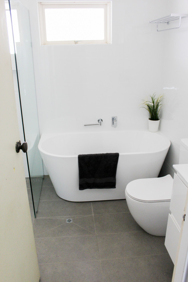 Inspiration for a mid-sized modern master bathroom in Perth with flat-panel cabinets, white cabinets, a freestanding tub, an open shower, a one-piece toilet, white tile, ceramic tile, white walls, porcelain floors, an integrated sink, solid surface benchtops, grey floor, an open shower and white benchtops.