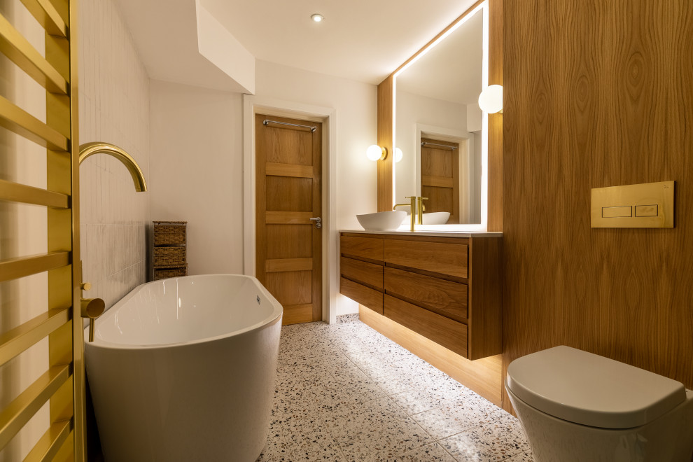 Inspiration for a large modern ensuite bathroom in London with recessed-panel cabinets, light wood cabinets, a freestanding bath, a walk-in shower, a wall mounted toilet, green tiles, porcelain tiles, white walls, porcelain flooring, a console sink, marble worktops, white floors, an open shower, white worktops, a feature wall, a single sink, a floating vanity unit, a wallpapered ceiling and wood walls.