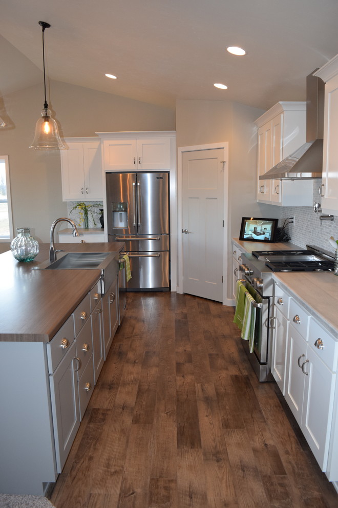 Large medium tone wood floor open concept kitchen photo with a drop-in sink, recessed-panel cabinets, white cabinets, laminate countertops, multicolored backsplash, ceramic backsplash, stainless steel appliances and an island