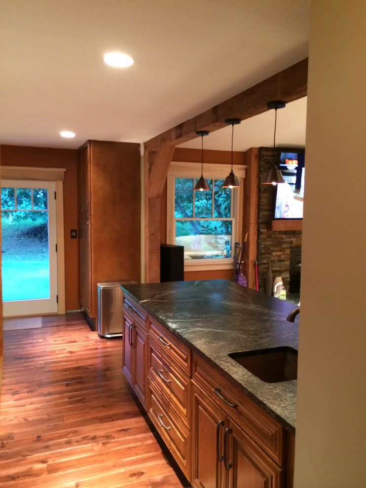 Large mountain style l-shaped medium tone wood floor eat-in kitchen photo in St Louis with a farmhouse sink, raised-panel cabinets, granite countertops, gray backsplash, glass tile backsplash, stainless steel appliances and a peninsula