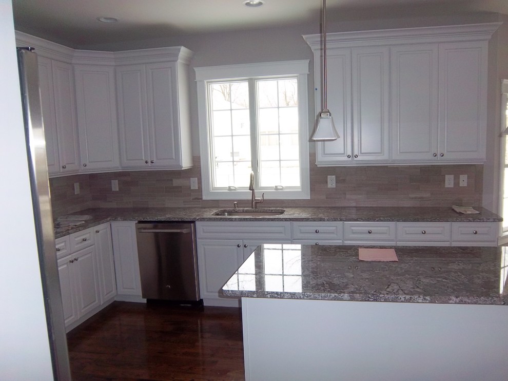 Large transitional u-shaped dark wood floor and brown floor kitchen photo with an undermount sink, raised-panel cabinets, white cabinets, granite countertops, gray backsplash, porcelain backsplash, stainless steel appliances, an island and gray countertops