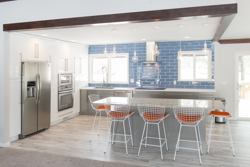 This is an example of a mid-sized beach style l-shaped kitchen in Other with a single-bowl sink, recycled glass benchtops, blue splashback, glass tile splashback, stainless steel appliances, ceramic floors, with island, flat-panel cabinets and grey cabinets.
