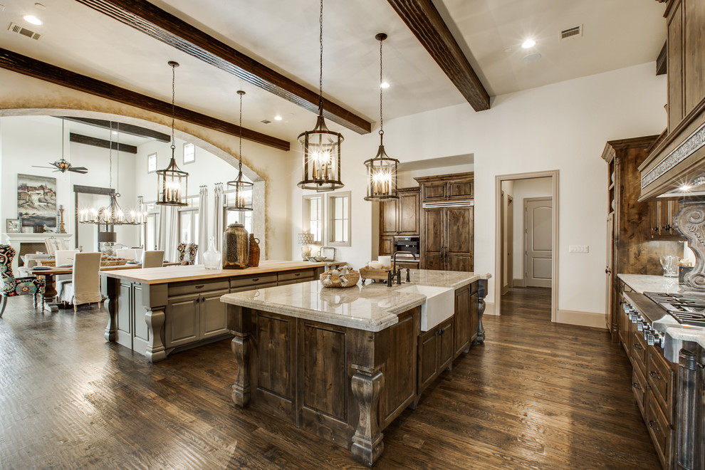 This is an example of an expansive mediterranean u-shaped open plan kitchen in Dallas with a farmhouse sink, raised-panel cabinets, dark wood cabinets, granite benchtops, beige splashback, stone tile splashback, panelled appliances, medium hardwood floors and multiple islands.