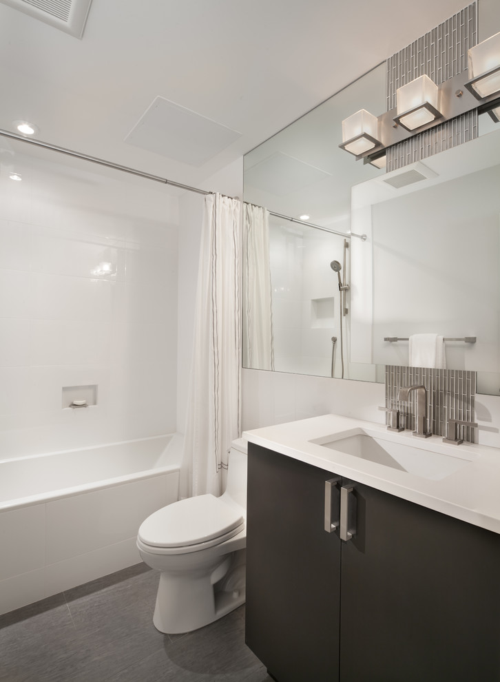 Photo of a mid-sized contemporary master bathroom in DC Metro with flat-panel cabinets, black cabinets, an alcove tub, white tile, white walls, vinyl floors, an undermount sink, a shower/bathtub combo, a one-piece toilet, ceramic tile and solid surface benchtops.