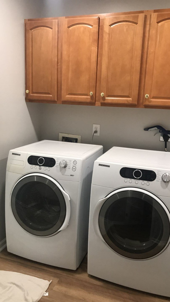 Large traditional laundry room in Indianapolis with recessed-panel cabinets, brown cabinets, grey walls, laminate floors, a side-by-side washer and dryer and brown floor.