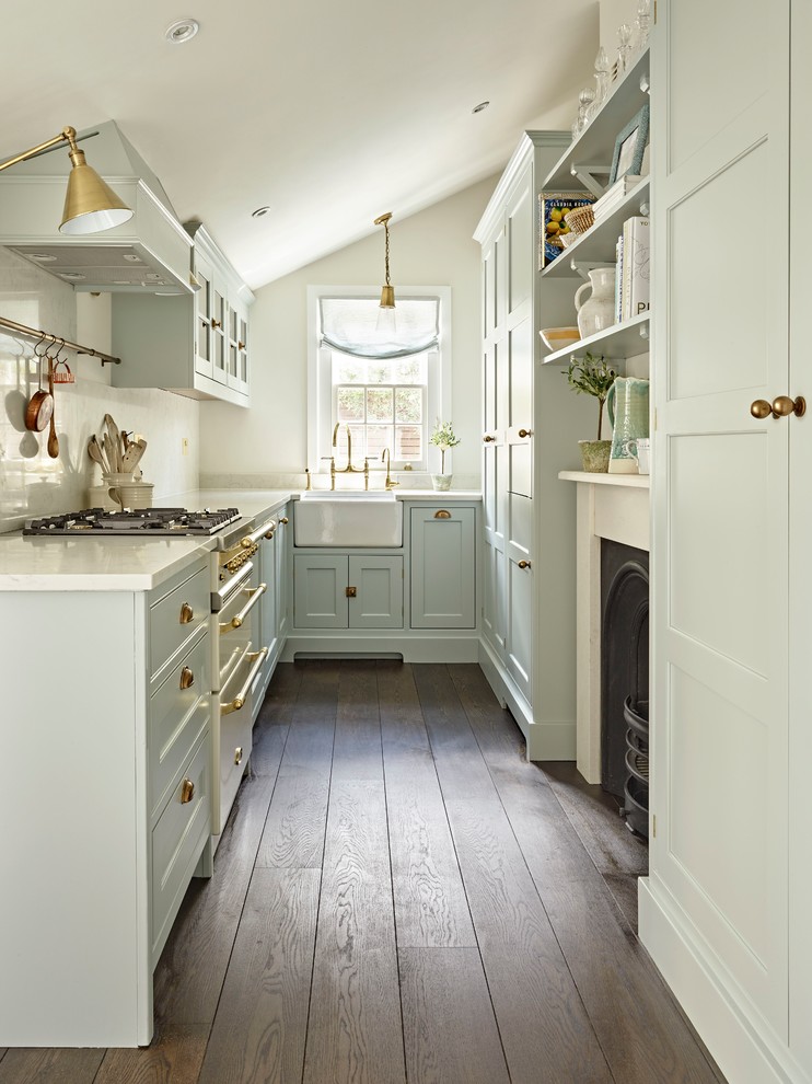 Small traditional l-shaped separate kitchen in London with a farmhouse sink, shaker cabinets, blue cabinets, white appliances, dark hardwood floors, brown floor, white benchtop, white splashback and no island.