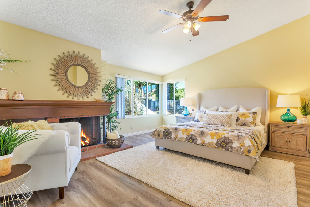 This is an example of a transitional bedroom in Los Angeles with yellow walls, medium hardwood floors, a standard fireplace, brown floor and vaulted.