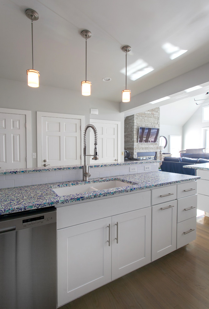 Design ideas for a mid-sized beach style galley open plan kitchen in Charleston with recycled glass benchtops, a double-bowl sink, white cabinets, white splashback, medium hardwood floors, a peninsula, flat-panel cabinets, subway tile splashback, stainless steel appliances and beige floor.