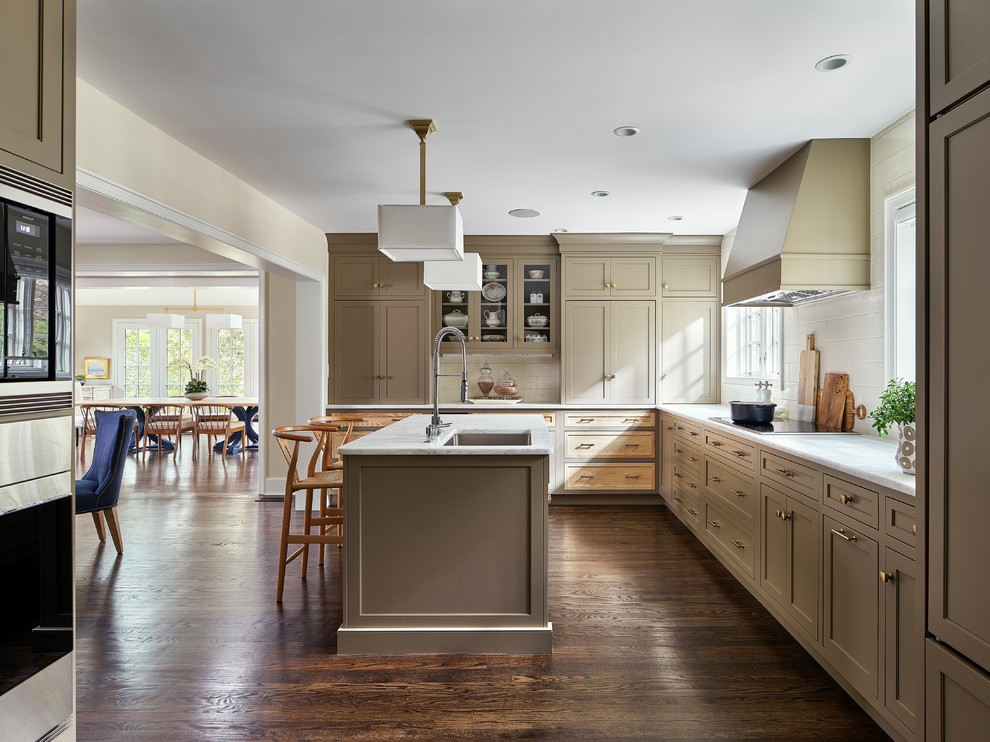 Large transitional l-shaped eat-in kitchen in Philadelphia with an undermount sink, marble benchtops, white splashback, porcelain splashback, stainless steel appliances, dark hardwood floors, with island, white benchtop, shaker cabinets, brown cabinets and brown floor.