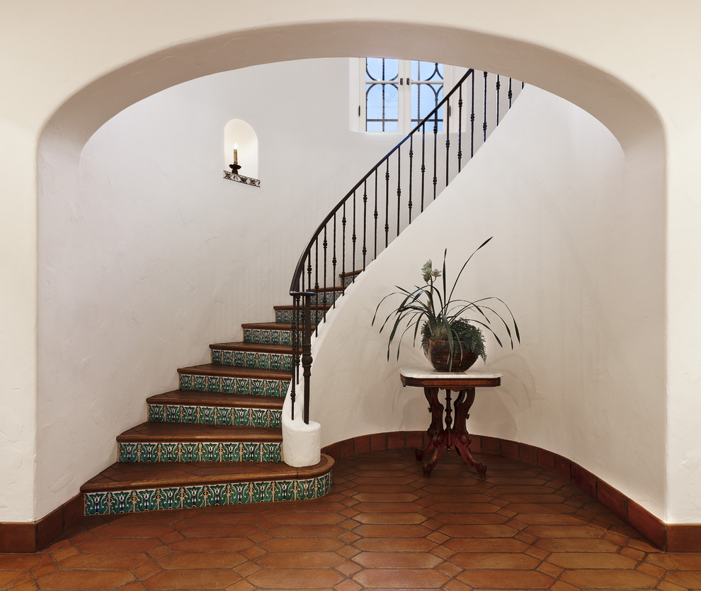 Photo of a large mediterranean terracotta curved staircase in Santa Barbara with tile risers and metal railing.