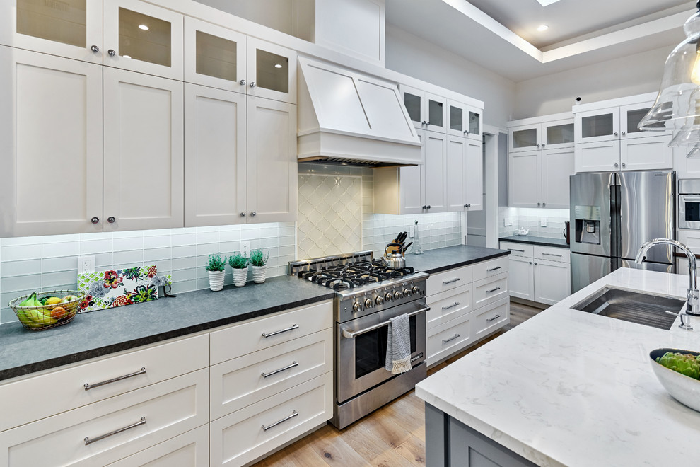 Photo of a mid-sized transitional l-shaped open plan kitchen in San Francisco with an undermount sink, shaker cabinets, white cabinets, quartz benchtops, grey splashback, glass tile splashback, stainless steel appliances, light hardwood floors and with island.