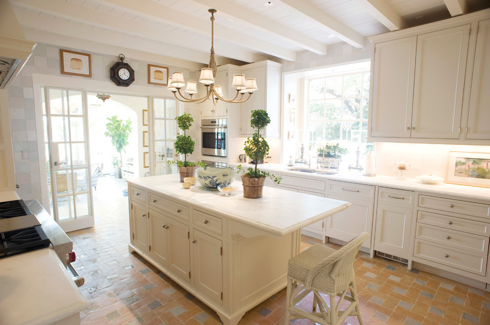 Mid-sized beach style u-shaped separate kitchen in Dallas with white cabinets, marble benchtops, ceramic splashback, panelled appliances, terra-cotta floors, with island, beige floor, a double-bowl sink, recessed-panel cabinets and grey splashback.