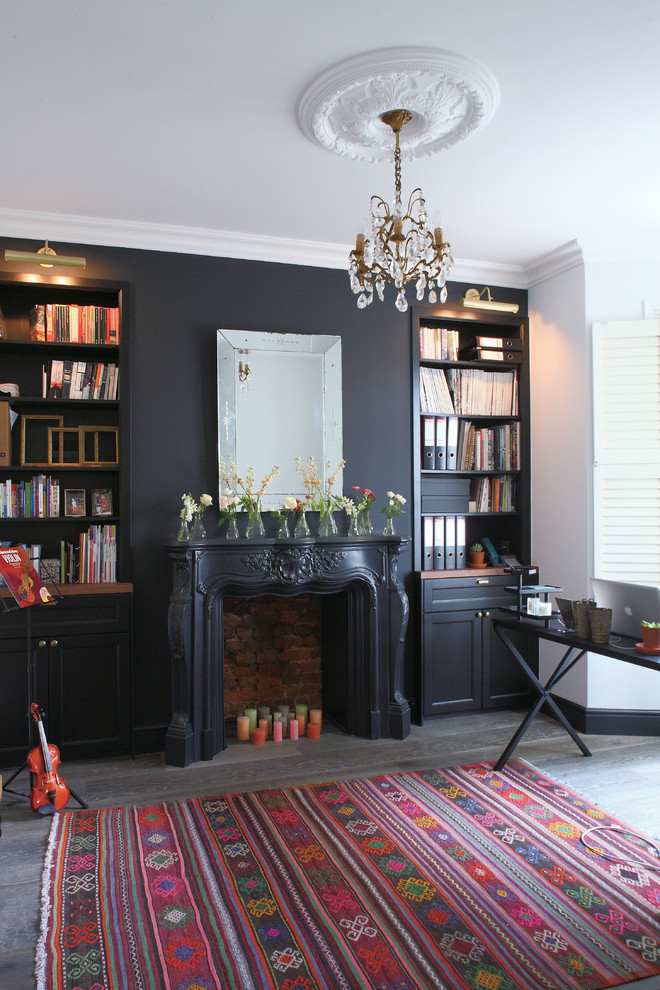 This is an example of a traditional home office in London with black walls, dark hardwood floors, a standard fireplace, a plaster fireplace surround, a freestanding desk and black floor.
