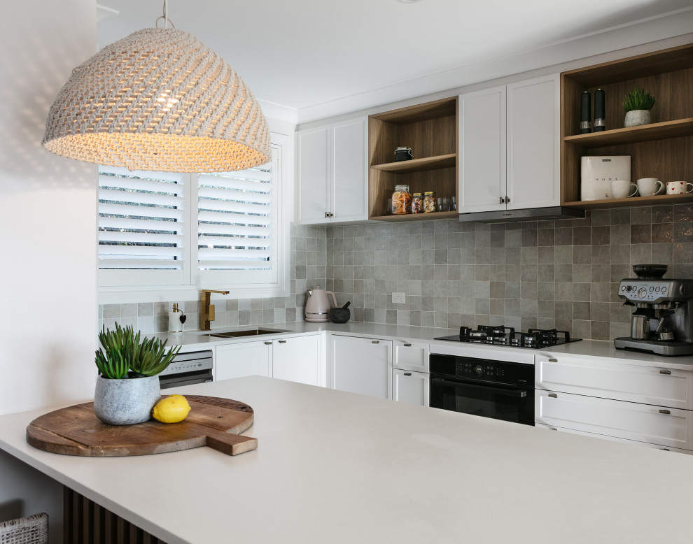 Design ideas for a mid-sized mediterranean u-shaped open plan kitchen in Sydney with a drop-in sink, shaker cabinets, white cabinets, quartz benchtops, multi-coloured splashback, ceramic splashback, black appliances, light hardwood floors, with island, beige floor and grey benchtop.