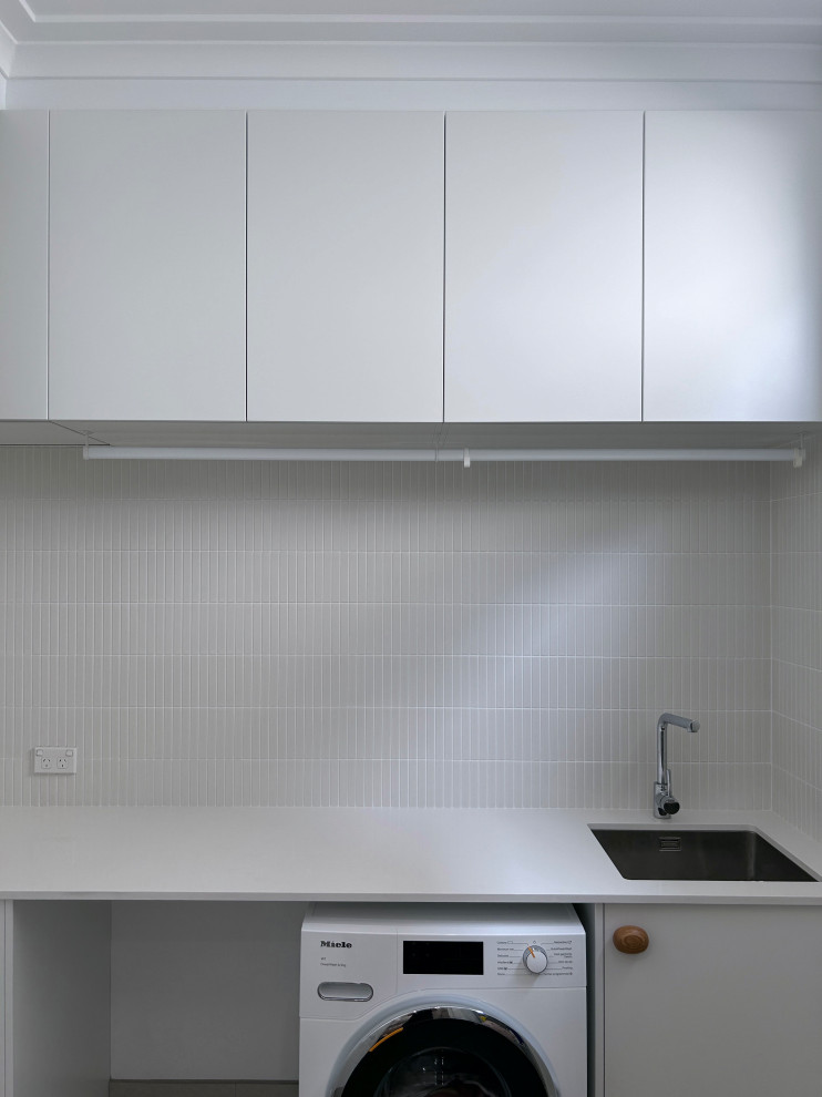Design ideas for a small modern l-shaped dedicated laundry room in Sydney with a single-bowl sink, flat-panel cabinets, white cabinets, quartz benchtops, green splashback, ceramic splashback, white walls, ceramic floors, a side-by-side washer and dryer, grey floor and white benchtop.