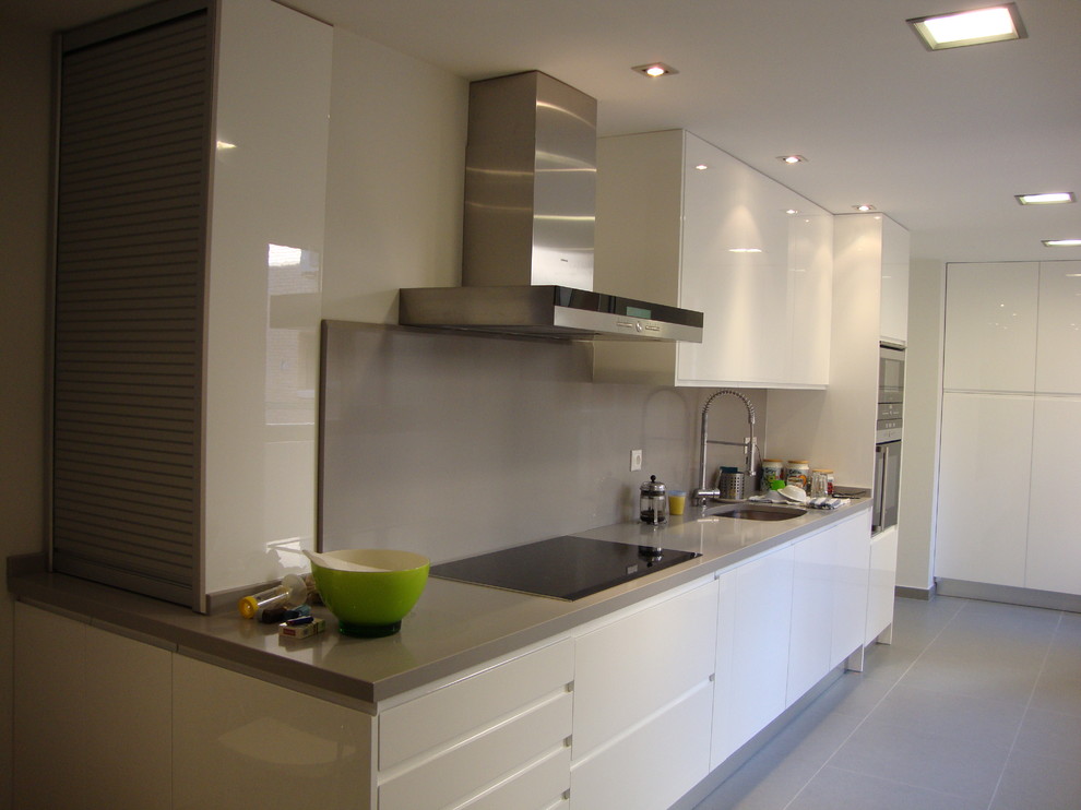 Design ideas for a mid-sized modern single-wall separate kitchen in Madrid with an undermount sink, white cabinets, ceramic floors, beaded inset cabinets, solid surface benchtops, grey splashback, limestone splashback, stainless steel appliances, no island and grey floor.