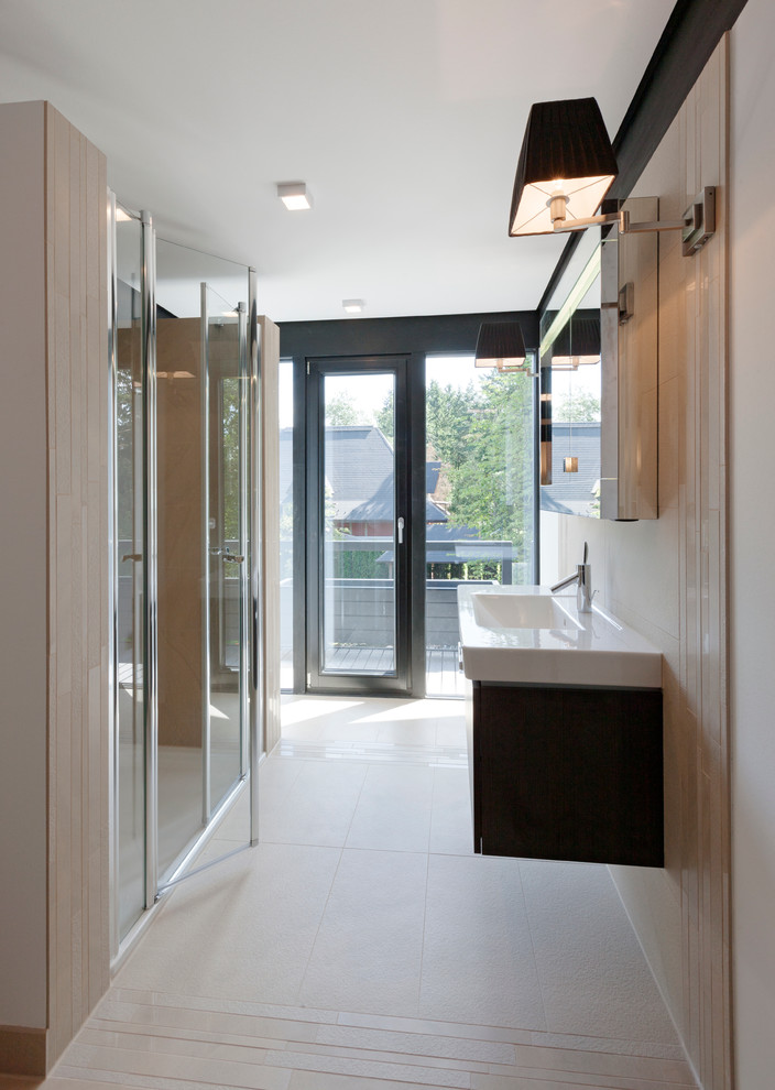 This is an example of a large contemporary bathroom in Stuttgart with flat-panel cabinets, black cabinets, an alcove shower, beige tile, beige walls, limestone floors and an integrated sink.
