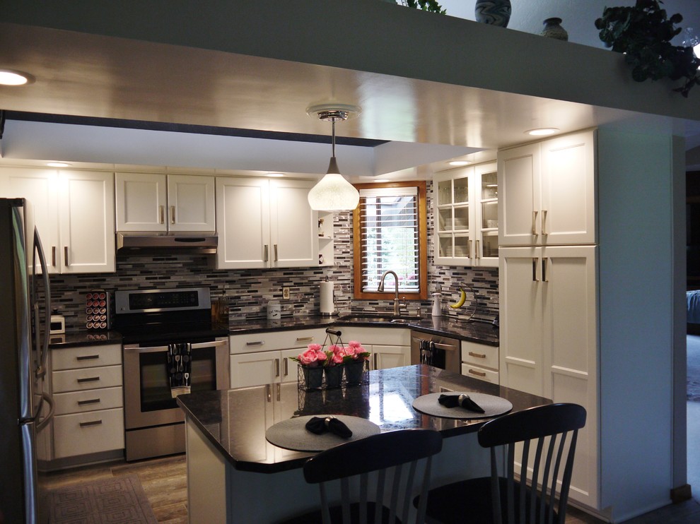 This is an example of a small transitional u-shaped kitchen in Grand Rapids with a double-bowl sink, recessed-panel cabinets, white cabinets, granite benchtops, multi-coloured splashback, glass tile splashback, stainless steel appliances and with island.