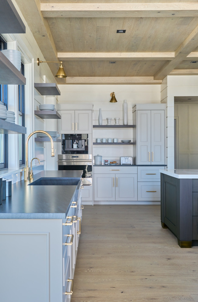 This is an example of an industrial u-shaped open plan kitchen in New York with a farmhouse sink, recessed-panel cabinets, blue cabinets, quartz benchtops, white splashback, shiplap splashback, stainless steel appliances, light hardwood floors, multiple islands, beige floor, white benchtop and wood.