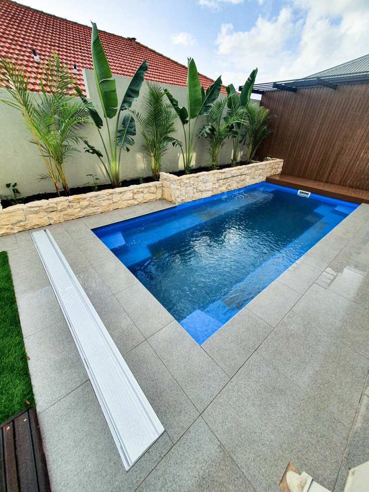 Modelo de piscina elevada pequeña rectangular en patio trasero con paisajismo de piscina y adoquines de piedra natural