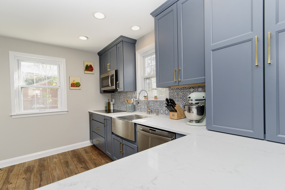 Enclosed kitchen - mid-sized transitional u-shaped vinyl floor and brown floor enclosed kitchen idea in Baltimore with a farmhouse sink, recessed-panel cabinets, blue cabinets, quartz countertops, blue backsplash, stainless steel appliances, a peninsula and white countertops