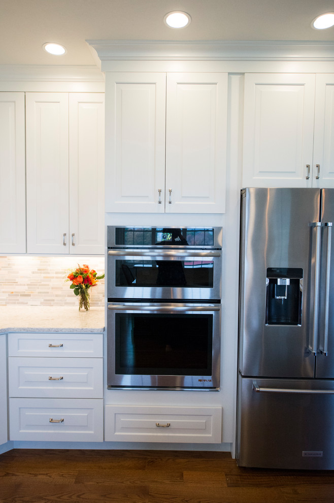 Eat-in kitchen - transitional l-shaped medium tone wood floor eat-in kitchen idea in Boston with white cabinets, granite countertops, gray backsplash, stainless steel appliances and an island