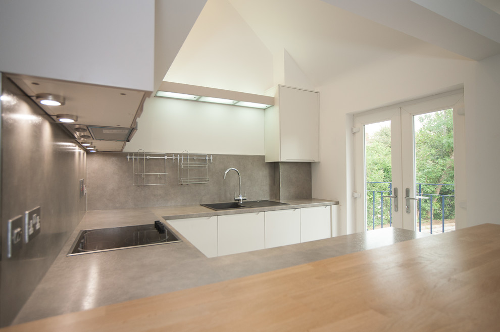 This is an example of a mid-sized contemporary u-shaped eat-in kitchen in Hertfordshire with a drop-in sink, flat-panel cabinets, white cabinets, grey splashback, slate splashback, stainless steel appliances, ceramic floors, a peninsula and grey floor.
