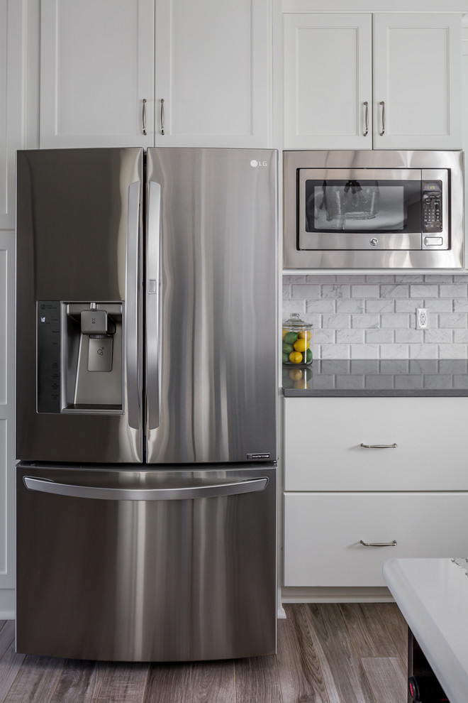 Inspiration for a mid-sized transitional l-shaped ceramic tile and gray floor eat-in kitchen remodel with an undermount sink, shaker cabinets, white cabinets, quartz countertops, white backsplash, marble backsplash, stainless steel appliances, an island and gray countertops