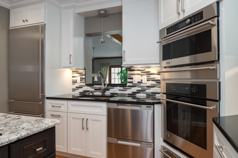 Example of a transitional l-shaped light wood floor eat-in kitchen design in St Louis with an undermount sink, shaker cabinets, white cabinets, quartz countertops, metallic backsplash, glass tile backsplash, stainless steel appliances and an island