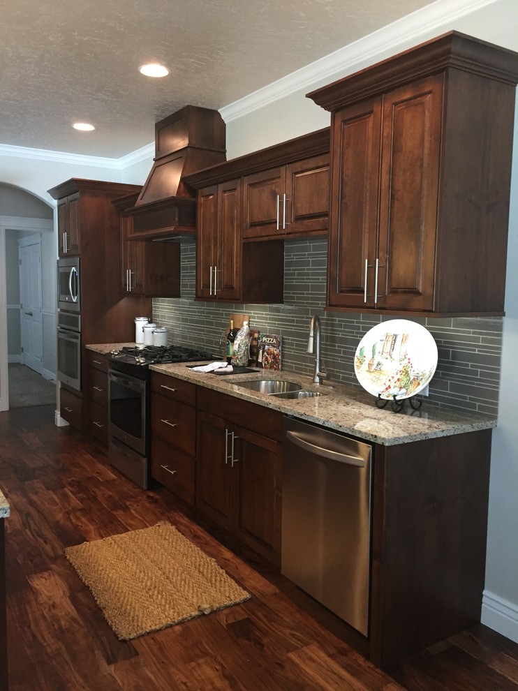 Open concept kitchen - mid-sized rustic l-shaped dark wood floor open concept kitchen idea in Boise with an undermount sink, raised-panel cabinets, dark wood cabinets, granite countertops, gray backsplash, glass tile backsplash, stainless steel appliances and an island