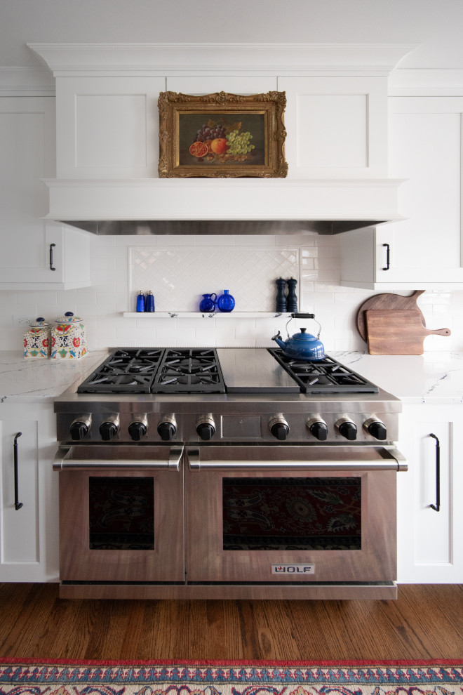 Foto på ett mellanstort vintage vit kök, med en undermonterad diskho, skåp i shakerstil, blå skåp, bänkskiva i kvarts, vitt stänkskydd, stänkskydd i keramik, rostfria vitvaror, mellanmörkt trägolv, en köksö och brunt golv