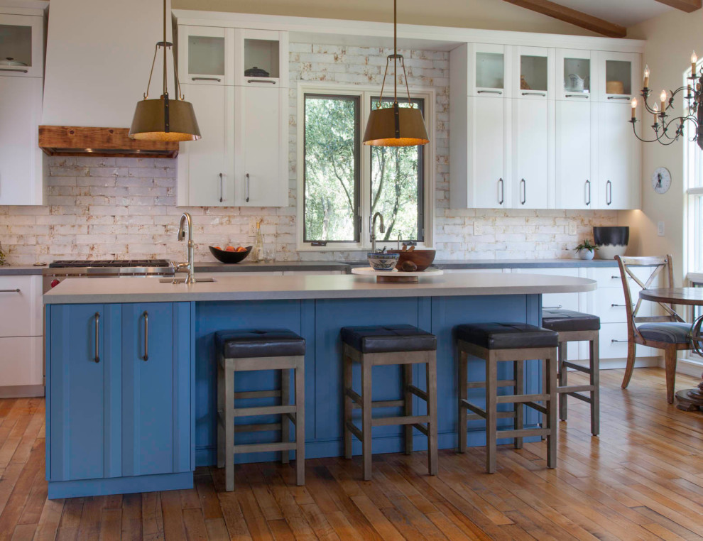 Mid-sized country l-shaped open plan kitchen in Denver with a farmhouse sink, flat-panel cabinets, blue cabinets, quartz benchtops, white splashback, cement tile splashback, stainless steel appliances, medium hardwood floors, with island, beige floor and grey benchtop.