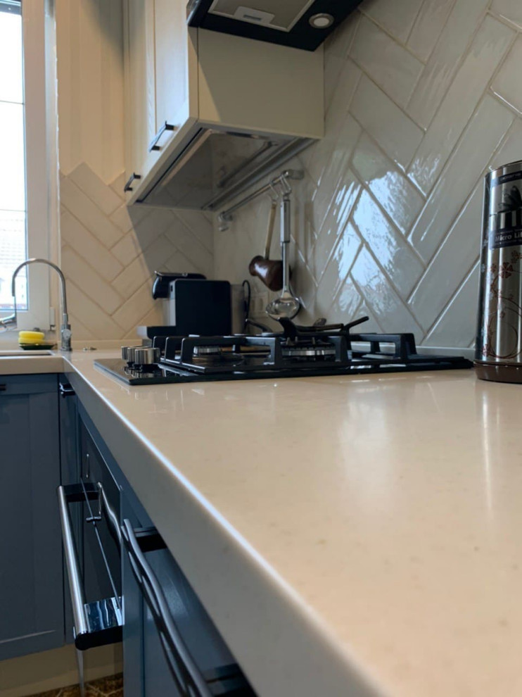 Mid-sized transitional u-shaped eat-in kitchen in Moscow with an undermount sink, raised-panel cabinets, blue cabinets, solid surface benchtops, white splashback, subway tile splashback, black appliances, ceramic floors, no island, brown floor and white benchtop.