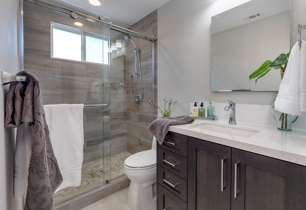 Photo of a mid-sized transitional master bathroom in Los Angeles with shaker cabinets, dark wood cabinets, an alcove shower, a two-piece toilet, gray tile, porcelain tile, grey walls, porcelain floors, an undermount sink, engineered quartz benchtops, grey floor and a sliding shower screen.
