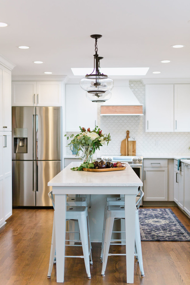 Example of a mid-sized transitional u-shaped medium tone wood floor and brown floor open concept kitchen design with an undermount sink, shaker cabinets, white cabinets, quartz countertops, white backsplash, porcelain backsplash, stainless steel appliances, an island and white countertops