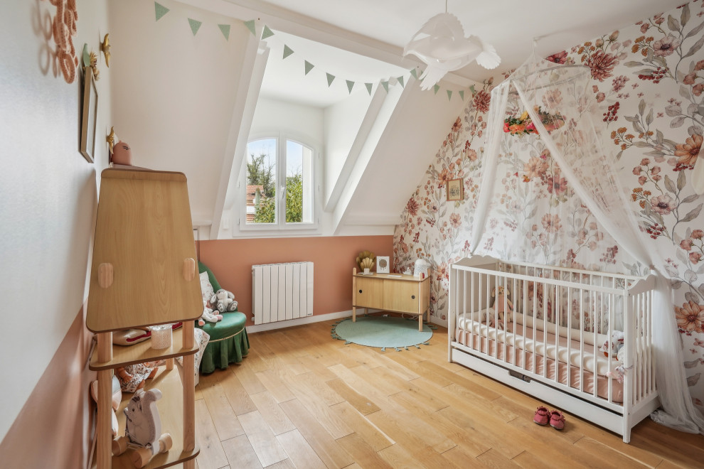 Cette image montre une chambre de bébé fille nordique avec un mur multicolore, un sol en bois brun, un sol marron et du papier peint.