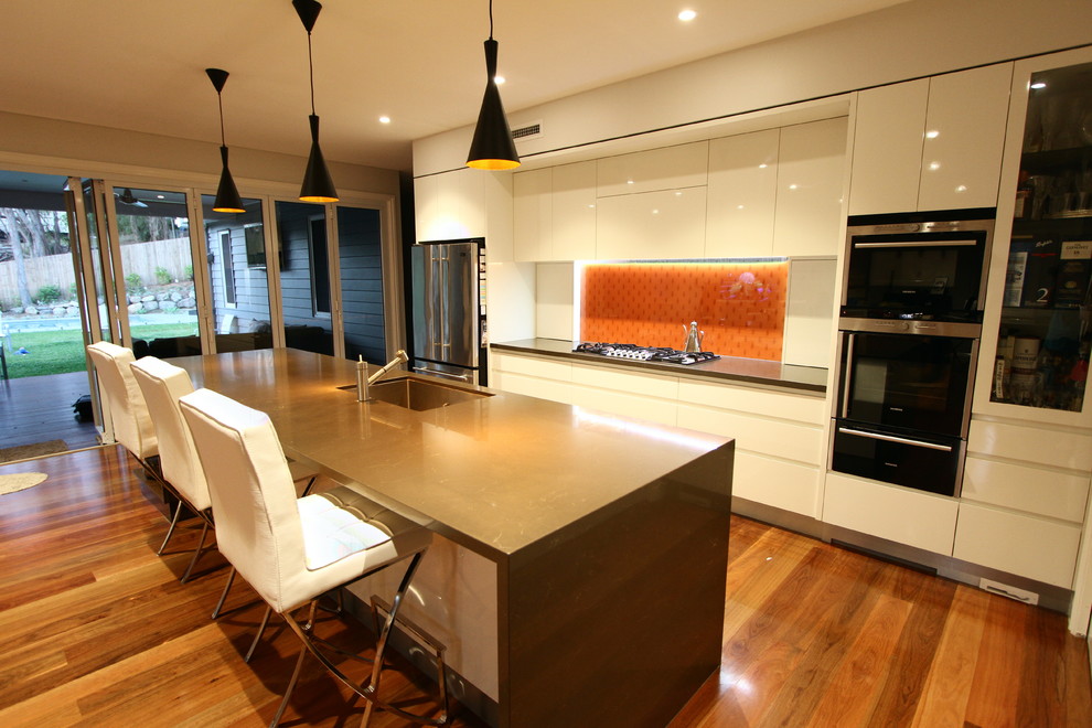 Mid-sized modern galley eat-in kitchen in Brisbane with an undermount sink, flat-panel cabinets, white cabinets, quartz benchtops, orange splashback, glass sheet splashback, stainless steel appliances and with island.