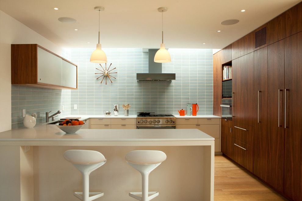 Photo of a large midcentury u-shaped kitchen in Los Angeles with an undermount sink, flat-panel cabinets, dark wood cabinets, blue splashback, stainless steel appliances, medium hardwood floors, a peninsula, brown floor and white benchtop.