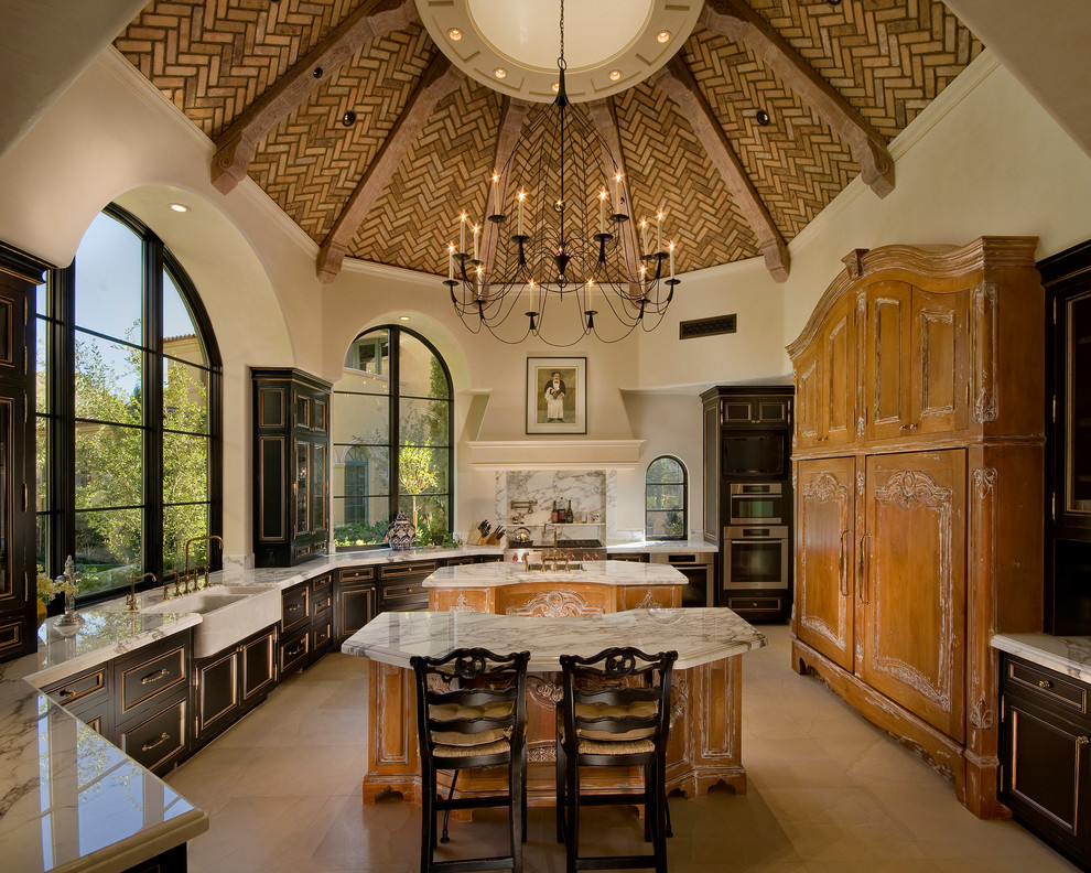 Expansive mediterranean u-shaped kitchen in Phoenix with a farmhouse sink, recessed-panel cabinets, dark wood cabinets, stainless steel appliances and multiple islands.