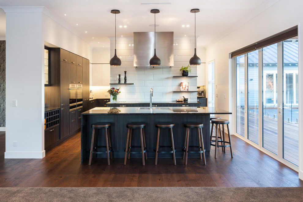 Design ideas for a large modern galley eat-in kitchen in Christchurch with dark wood cabinets, granite benchtops, white splashback, ceramic splashback, stainless steel appliances, medium hardwood floors, with island, brown floor, black benchtop and a double-bowl sink.
