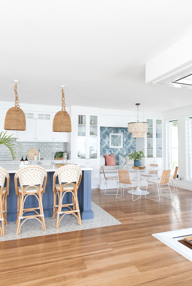 This is an example of a large beach style l-shaped eat-in kitchen in Gold Coast - Tweed with a single-bowl sink, shaker cabinets, white cabinets, quartz benchtops, green splashback, porcelain splashback, stainless steel appliances, porcelain floors, with island, beige floor and white benchtop.