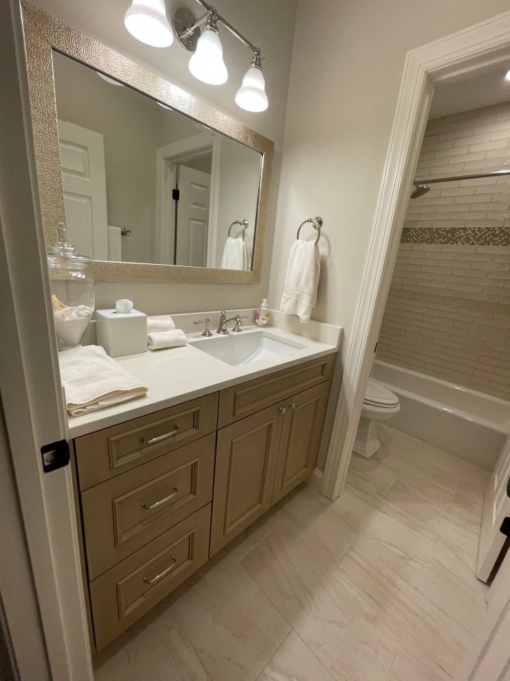 Example of a mid-sized white tile and porcelain tile ceramic tile, brown floor and single-sink alcove bathtub design in DC Metro with recessed-panel cabinets, light wood cabinets, a two-piece toilet, an undermount sink, quartz countertops, white countertops, a niche and a built-in vanity