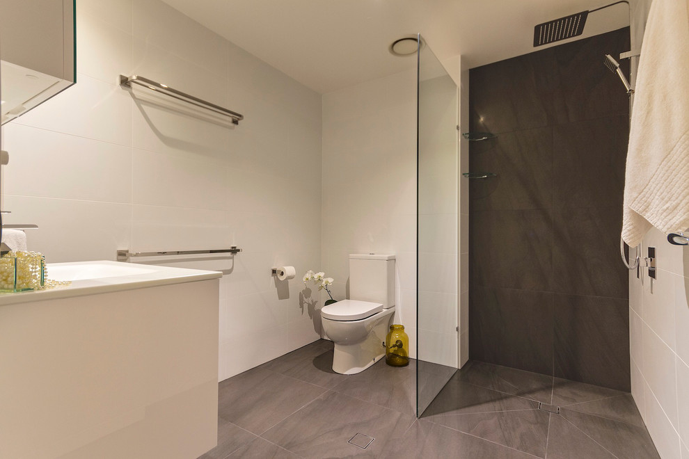Inspiration for a mid-sized contemporary wet room bathroom in Brisbane with white cabinets, a two-piece toilet, gray tile, stone slab, white walls, ceramic floors, an integrated sink and recycled glass benchtops.