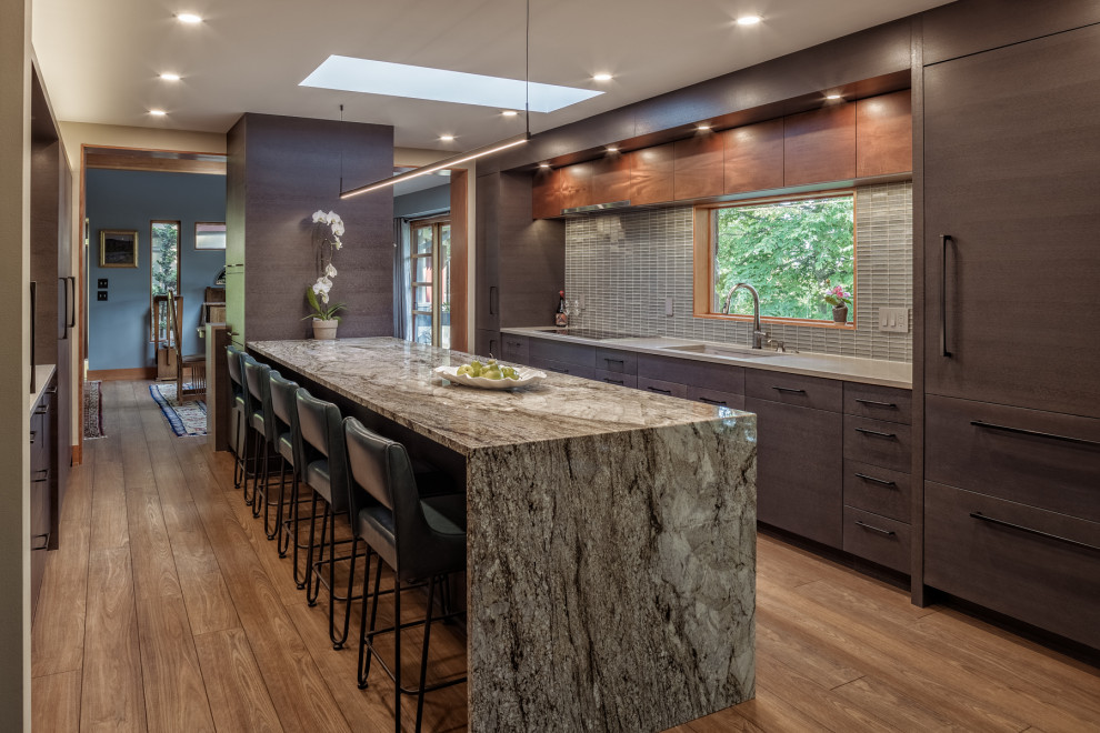 Design ideas for a mid-sized eclectic galley open plan kitchen in Detroit with an undermount sink, flat-panel cabinets, dark wood cabinets, granite benchtops, grey splashback, glass tile splashback, panelled appliances, vinyl floors, with island, beige floor and grey benchtop.