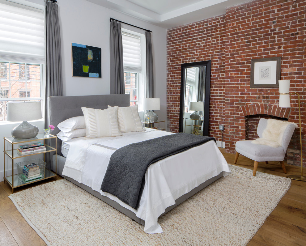 This is an example of a transitional master bedroom in New York with grey walls, light hardwood floors, a standard fireplace and a brick fireplace surround.