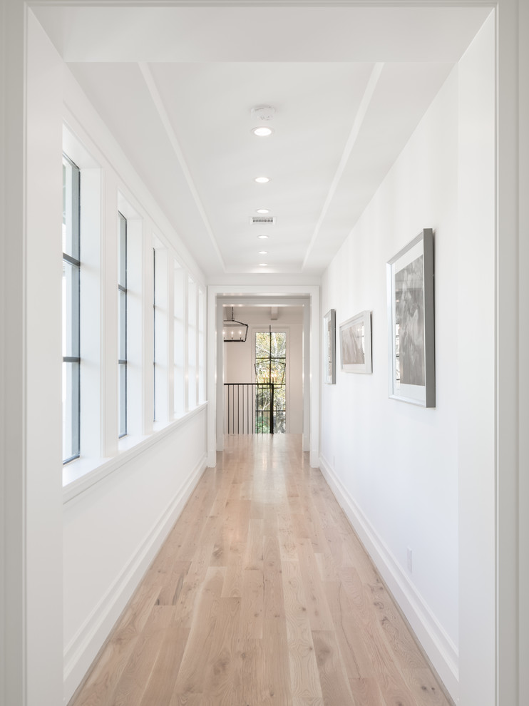 This is an example of a mid-sized transitional hallway in Houston with white walls, light hardwood floors and beige floor.
