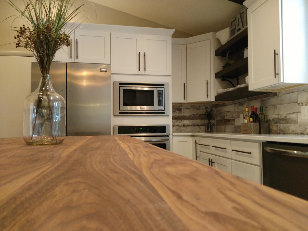 Example of a mid-sized transitional l-shaped dark wood floor and brown floor eat-in kitchen design with a farmhouse sink, shaker cabinets, white cabinets, wood countertops, gray backsplash, marble backsplash, stainless steel appliances and an island