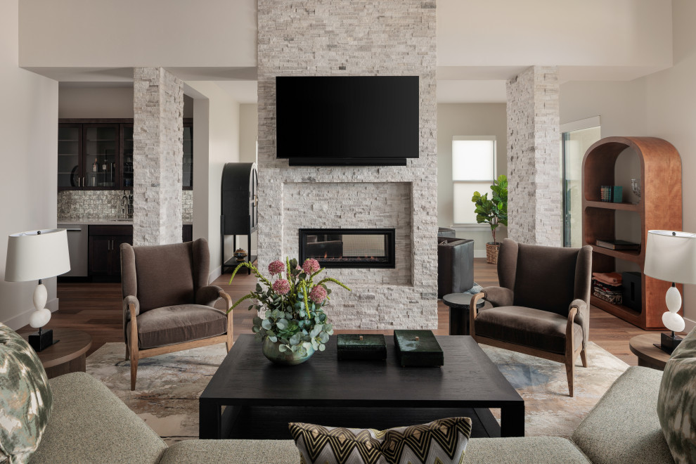 Mid-sized transitional open concept medium tone wood floor and brown floor living room photo with a bar, white walls, a two-sided fireplace, a stone fireplace and a wall-mounted tv