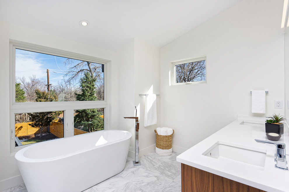 This is an example of a mid-sized modern master bathroom in Denver with flat-panel cabinets, medium wood cabinets, a freestanding tub, white walls, marble floors, an undermount sink, engineered quartz benchtops and grey floor.